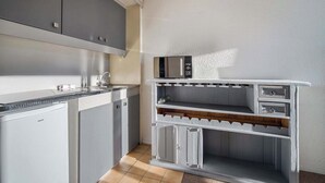 Eine kleine Küche mit grauen Schränken, einer eingebauten Mikrowelle und einem kleinen Kühlschrank.