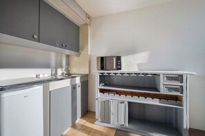 Uma cozinha compacta com armários cinzas, micro-ondas embutido e uma geladeira pequena.