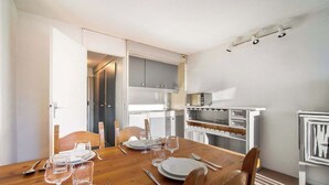 Ein Essbereich mit einem Holztisch, gedeckt für vier Personen, eine Küche mit weißen Schränken und ein kleiner Kühlschrank.