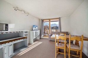 Une pièce comprenant une table et des chaises, un canapé, un petit coin cuisine et une grande fenêtre donnant sur les montagnes.