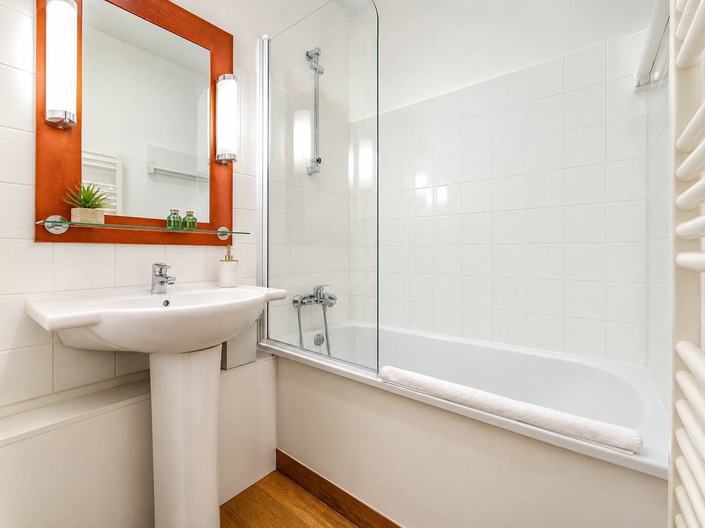 Ein Badezimmer mit weißem Waschbecken, Spiegel und einer Duschkabine aus Glas.