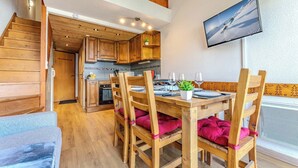 Ein Holzinterieur mit einem für vier Personen gedeckten Esstisch, Holzstühlen, einer Küchenzeile und einem an der Wand befestigten Fernseher.
