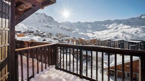 A wooden balcony overlooking a snow-covered mountain town with buildings and a clear sky. - Luxurious Apartment with Ski-In and Out Access in Centre (Val Thorens)