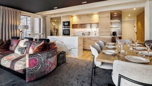A modern living room with a sofa, a dining table set for a meal, and a kitchen area with a marble countertop. - Luxurious Apartment with Ski-In and Out Access in Centre (Val Thorens)