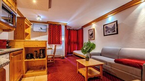 A cozy living room with a red carpet, wooden furniture, a grey sofa, and a television on the wall. - Slope-Side Apt w/Balcony & Views (Val Thorens)