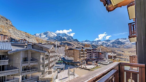 A mountain town with traditional wooden buildings, a central square, and snow-capped mountains in the background. - Slope-Side Apt w/Balcony & Views (Val Thorens)