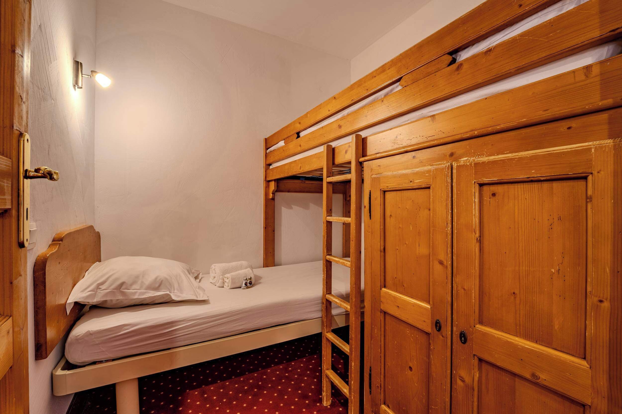 Ein Einzelbett mit Holzkopfende, einer Holzleiter und einem roten Teppich mit weißen Punkten.