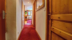 A hallway with a red carpet, wooden doors, and a view into a room with a plant and a red curtain. - Slope-Side Apt w/Balcony & Views (Val Thorens)