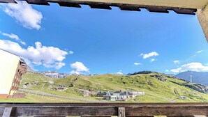 Ein Blick auf eine gebirgige Landschaft mit blauem Himmel, einem hölzernen Zaun im Vordergrund und einigen Gebäuden in der Ferne.