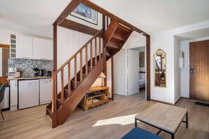Une cuisine moderne avec un escalier en bois, des armoires blanches et un mur recouvert de carreaux.