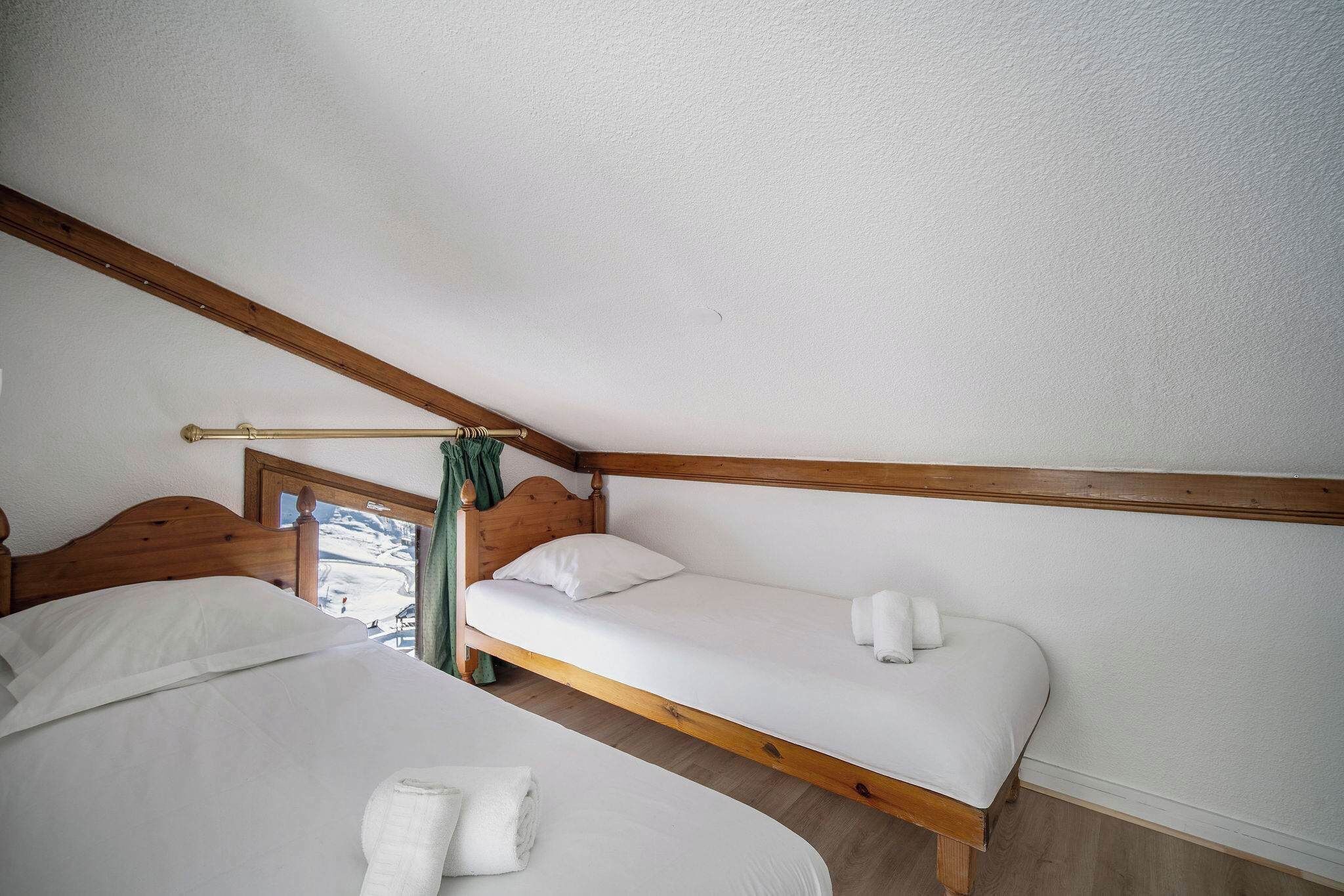 Une chambre avec deux lits, des poutres en bois et une fenêtre avec des rideaux.