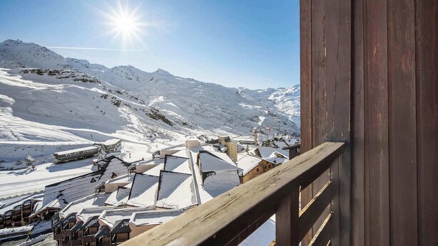 Ett snötäckt berglandskap med en träbyggnad och en skidlift i bakgrunden.