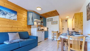 Ett mysigt rum med en blå soffa, träväggar, en köksdel och ett matbord dukat för två personer.
