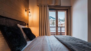 Ein Schlafzimmer mit einem Holzkopfende, einem Bett mit weißer und dunkelgrauer Decke, einem Nachttisch mit Lampe und einem Fenster mit Vorhängen.