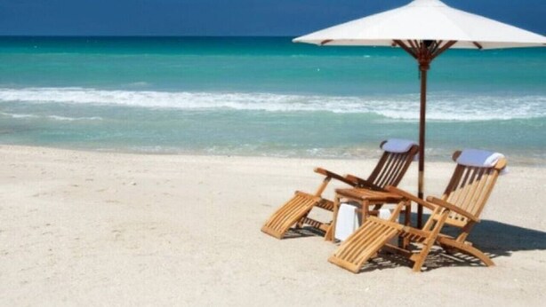 Una spiaggia con due lettini di legno e un ombrellone bianco.