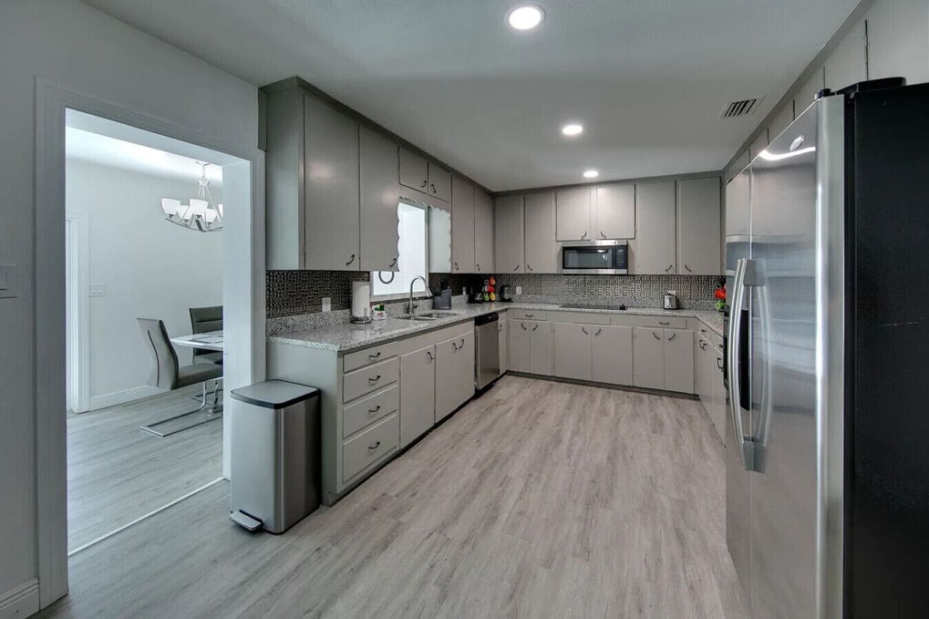 A modern kitchen with grey cabinets, a stainless steel refrigerator, a microwave, and a dining area with a table and chairs.