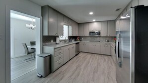 Una cucina moderna con mobili grigi, un frigorifero in acciaio inossidabile, un forno a microonde e un'area pranzo con tavolo e sedie.