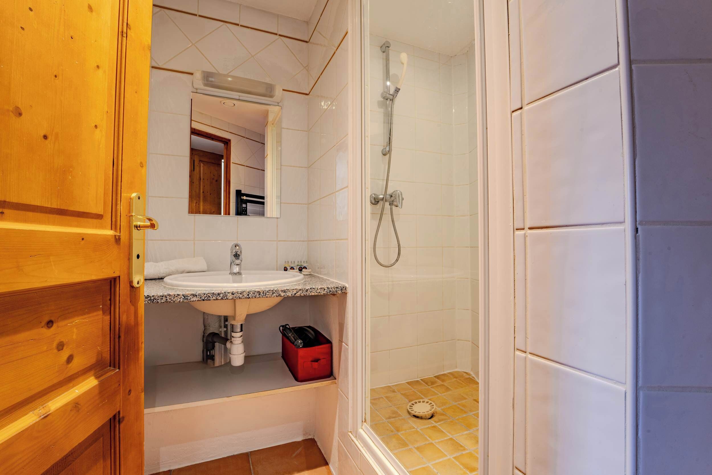 Une salle de bain avec une porte en bois, un lavabo, un miroir et un espace douche.