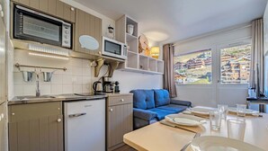 Cozinha compacta com micro-ondas, chaleira e mini-geladeira. Mesa de jantar posta com pratos e copos.