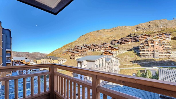 Varanda de madeira com vista para uma área montanhosa e vários edifícios de madeira, sugerindo um ambiente de resort ou pousada.
