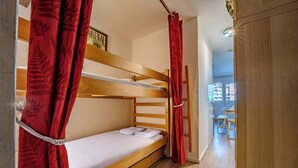 Uma cama beliche com cortinas vermelhas, uma cabeceira de madeira e uma pequena mesa ao fundo.