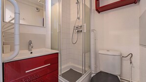 Casa de banho com chuveiro em cabine de vidro, sanita branca e toucador vermelho com gavetas.