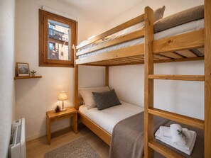 Ein Schlafraum mit Etagenbett, Fenster, Nachttisch, Lampe und einem kleinen Regal mit einem Bild.