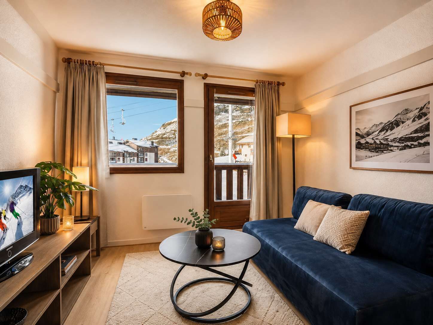 Un salon chaleureux avec un canapé bleu, un téléviseur, une petite table sur laquelle est posée une plante, et une fenêtre avec des rideaux.
