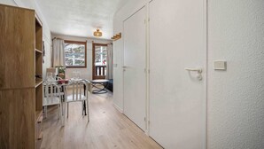 Una habitación compacta con un armario de madera, una mesa de comedor con sillas, una pequeña mesa redonda y una puerta que da a un área exterior.