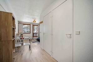 Ein gemütlicher Raum mit einem Holzschrank, einem Esstisch mit Stühlen, einem kleinen runden Tisch und einer Tür zu einem Außenbereich.