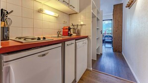Cozinha estreita com armários brancos, bancada vermelha e vista para uma sala de jantar com mesa e cadeiras.