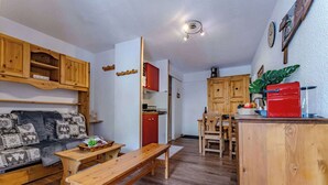 A cozy living room with a sofa, wooden bench, and a dining area with a red refrigerator and wooden cabinets. - Resort Access Flat (Val Thorens)