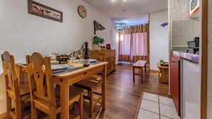 A dining area with wooden furniture, a clock, and a television. - Resort Access Flat (Val Thorens)
