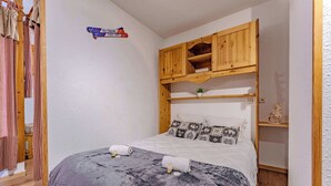 A small, cozy room with a bed, wooden shelves, and a checkered curtain. - Resort Access Flat (Val Thorens)
