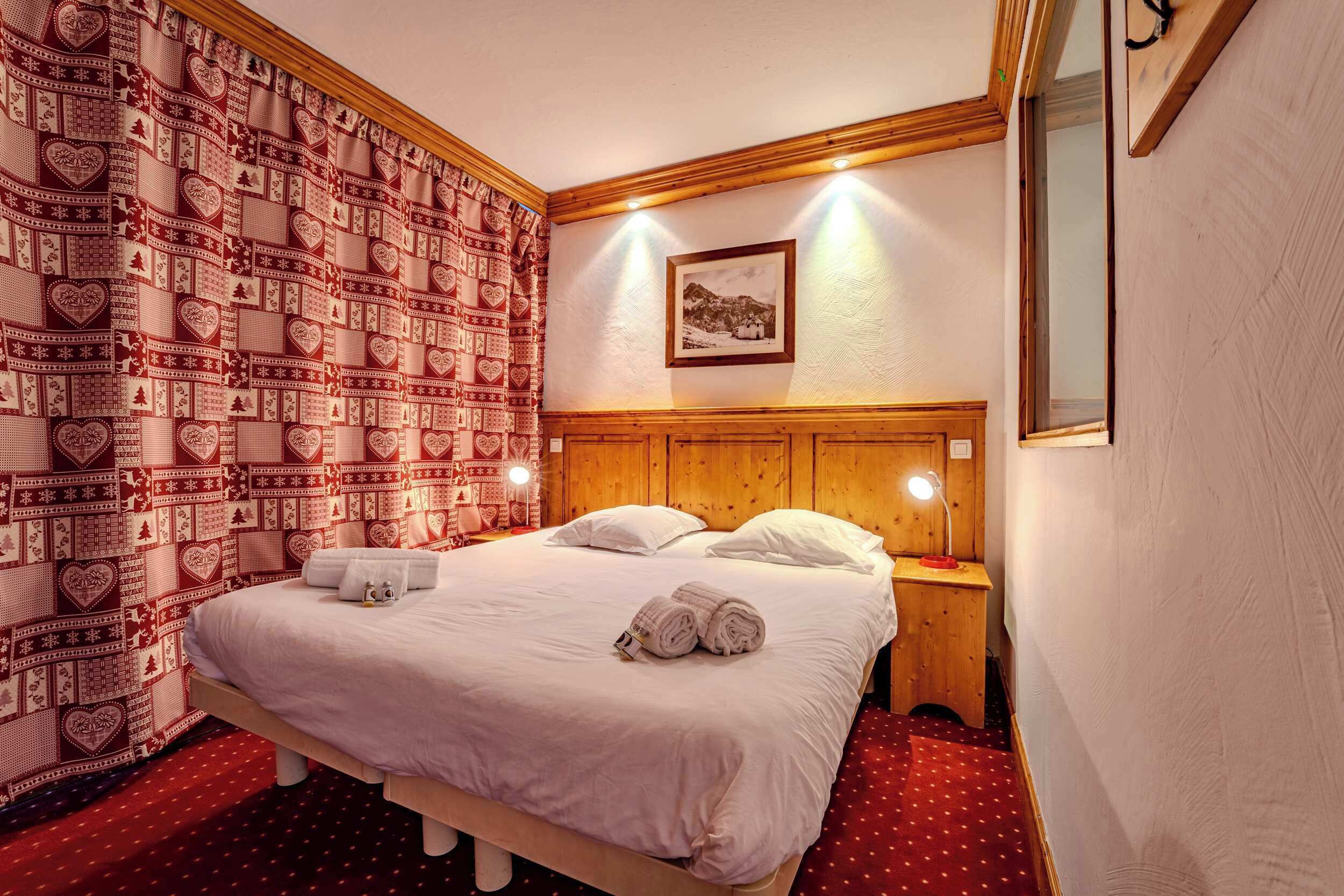 Un lit bien fait, avec du linge de lit blanc et des serviettes pliées, une tête de lit en bois et un tableau accroché au mur.
