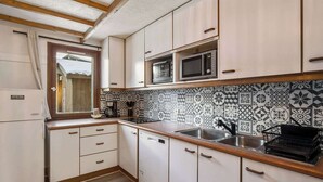 A compact kitchen with a microwave, sink, and a window with curtains. - Ski-In and Out Mountain View Escape 47 (Val Thorens)