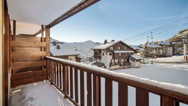 A wooden balcony with a snow-covered ground and a view of a mountain and buildings. - Ski-In and Out Mountain View Escape 47 (Val Thorens)