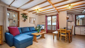 A cozy living room with a blue sofa, wooden coffee table, and a dining area with a wooden table and chairs. - Ski-In and Out Mountain View Escape 47 (Val Thorens)