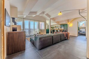 Amplia sala de estar con un sofá modular grande, un mueble de madera y una cocina al fondo.