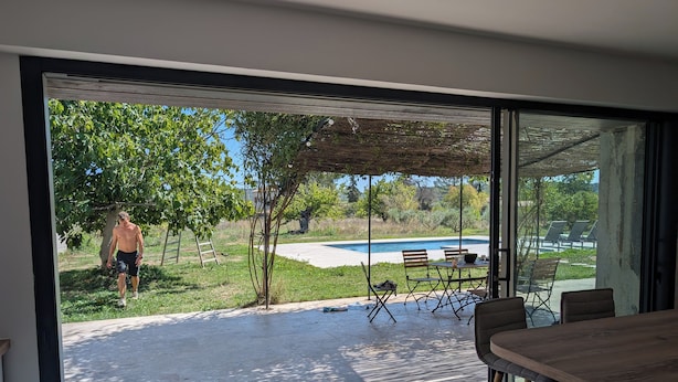 Un patio moderno al aire libre con puerta de vidrio que da a una zona de piscina, una mesa de madera y sillas.