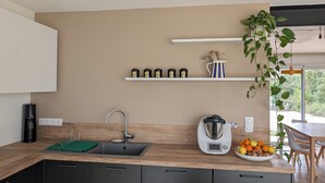 Una cocina moderna con encimera de madera, lavaplatos integrado, tetera y un cuenco con fruta.