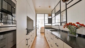 A modern kitchen with white cabinetry, black handles, and a black countertop. There is a vase with flowers on the countertop. - EXCEPTIONAL SETTING ON RUE BUCI TO EXPERIENCE PARIS AT FINEST, SAINT-GERMAIN (Paris)