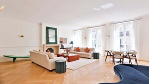 A spacious living room with a fireplace, a sofa set, a dining area, and large windows. - EXCEPTIONAL SETTING ON RUE BUCI TO EXPERIENCE PARIS AT FINEST, SAINT-GERMAIN (Paris)