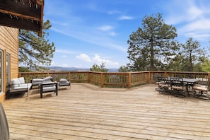 Eine Holzterrasse mit Gartenmöbeln, einem Tisch und Blick auf Bäume sowie ferne Berge.
