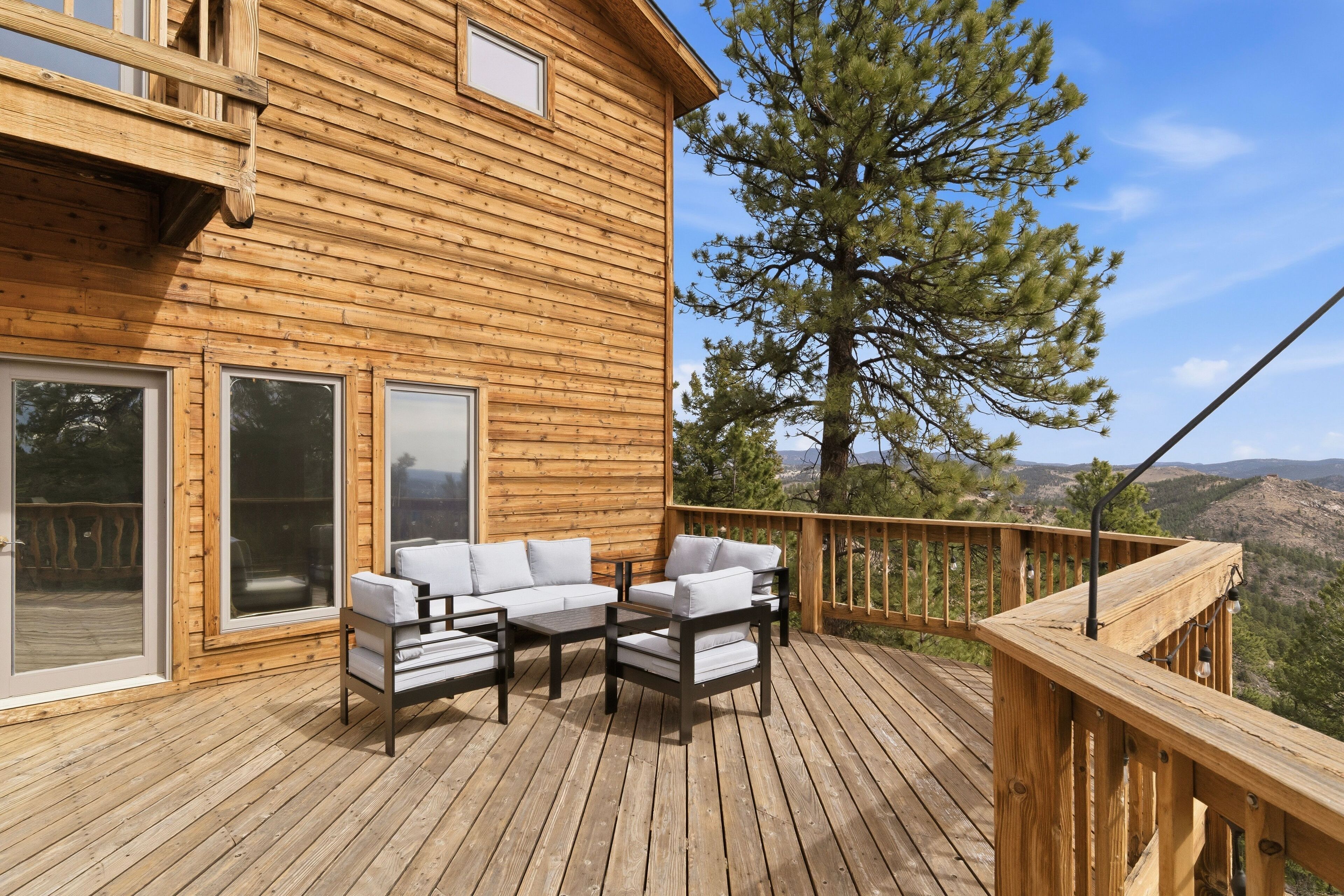 A wooden deck with outdoor furniture, a large window, and a view of the mountains.