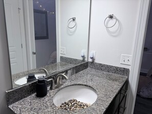 A bathroom with a granite countertop, a sink, a mirror, and a ring light. - Stylish Modern Studio, Steps from Dining & Entertainment (Charlotte)