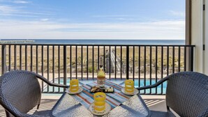 Un balcón con vista a la playa y al océano, una mesa con una botella de vino Amelia y dos sillas de mimbre.
