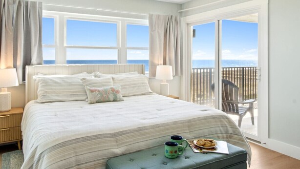 Un dormitorio con una cama grande, vista al mar a través de una puerta corrediza y un balcón con una silla.
