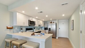 Cocina moderna con armarios blancos, un refrigerador de acero inoxidable y una isla central con taburetes.
