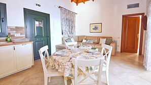 A dining area with a table set for four, a sofa, and a kitchen area with cabinets and a sink. - Villa Triton (Corfu)
